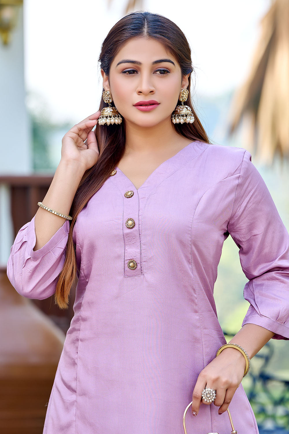 Woman in a light purple outfit standing outdoors with plants and furniture in the background